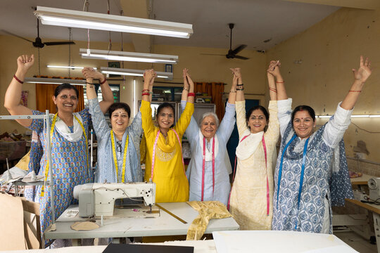 Confident Indian skilled women workers in a textile company raising their hands during a training session under the Skill India initiative. Female textile employees actively participating in workplace