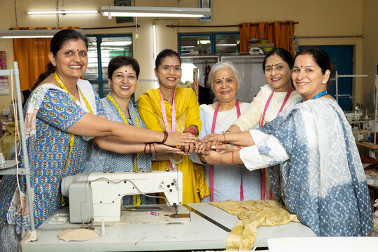 Group of confident Indian Skill India women workers standing together inside a textile company, joining hands as a symbol of teamwork, unity, trust, and women empowerment.