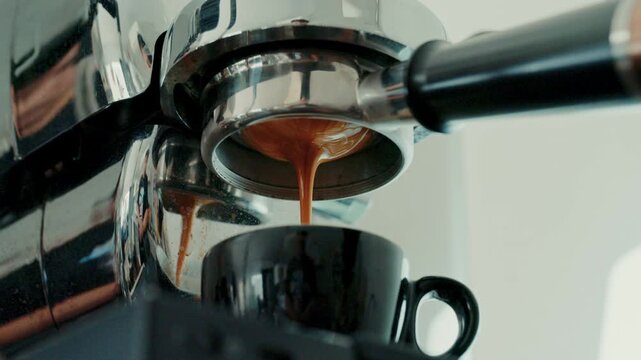 4K Pouring coffee stream from professional machine in cup. Barista man making double espresso, using filter holder. Flowing fresh ground coffee. Drinking roasted black coffee in the morning.