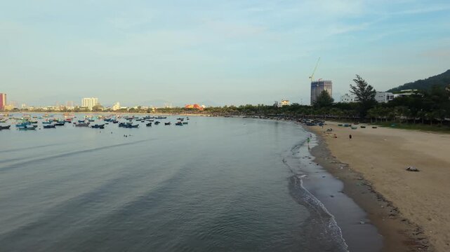 Low altitude drone flight following a peaceful beach with fishing boats and the Da Nang skyline at sunrise in Vietnam.
