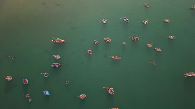 Vertical drone shot capturing colorful fishing boats floating on calm green water off the coast of Da Nang, Vietnam.