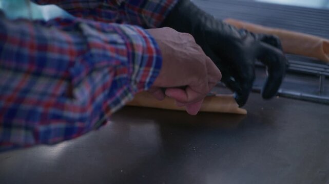Asian street food vendor preparing thin pancake rolled crepe with sausage on hot pan.