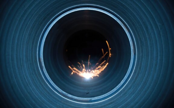 Industrial metal pipe welding with bright orange sparks, interior view of steel pipeline construction, blue metallic circular tunnel texture