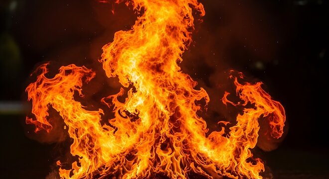 Bright orange flames burning in darkness. Intense fire blaze isolated on black background.