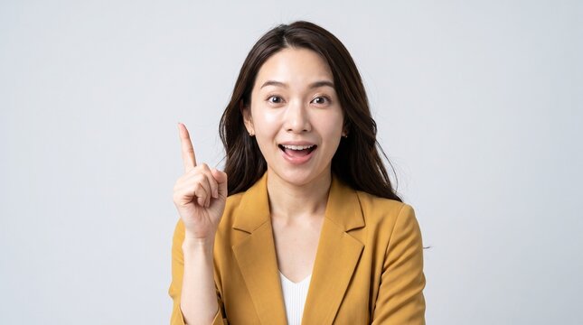 Studio shot of a surprised and happy Asian businesswoman pointing her index finger up in a eureka moment, having a great new idea or solution.