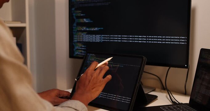 Software developer writing, reviewing and debugging source code across multiple screens using tablet and computer in modern workspace for software engineering, programming and application development.