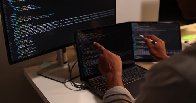 Software developer writing, reviewing and debugging source code across multiple screens using tablet and computer in modern workspace for software engineering, programming and application development.