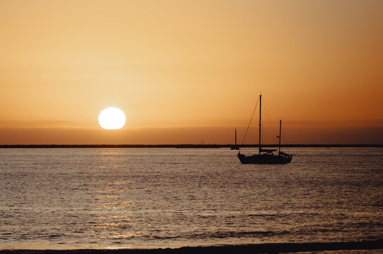 A serene sailboat gliding across calm waters at sunset, shadowed by a golden sky, evoking feelings of peace and exploration in a beautiful coastal landscape.
