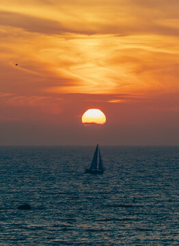 A captivating sailboat journeying across the water under a dramatic sunset sky, rich with vibrant colors and swirling clouds, creating an artistic visual experience.