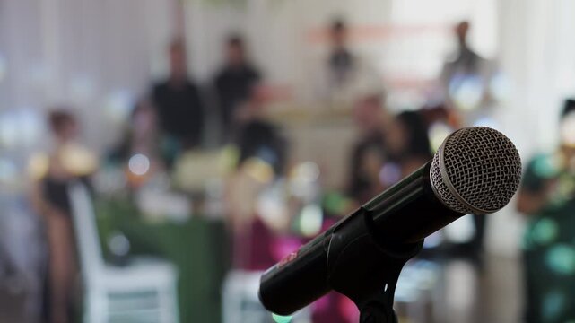 Professional microphone on stage with blurred audience during a conference, wedding reception or corporate event. Public speaking, presentation and live entertainment concept.
