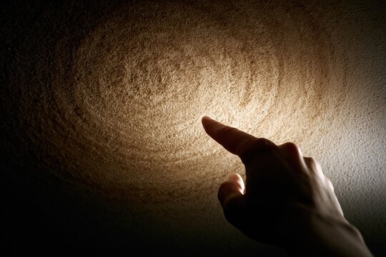 Human Finger Pointing at Illuminated Swirling Pattern on Textured Surface in Darkness