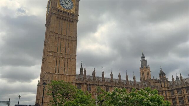 A tall Gothic clock tower rises above green trees beneath dramatic storm clouds