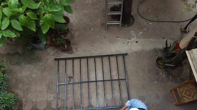 Young Man Putting On Work Gloves While Walking Beside Metal Bed Frame
