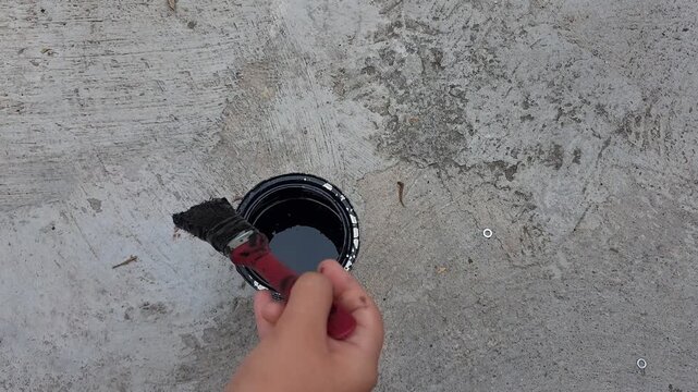 Child Hand Applying Black Paint with Brush to Metal Structure