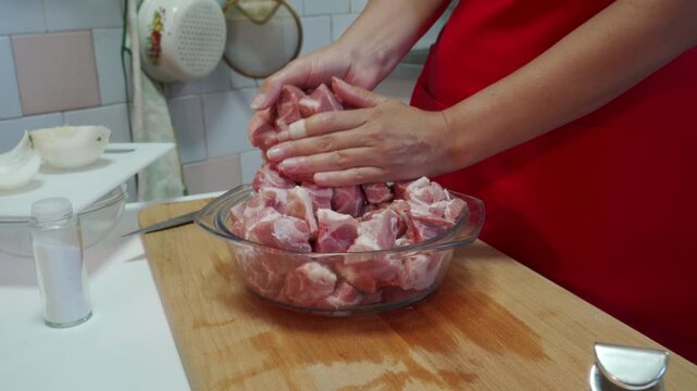 Hands preparing meat mixing and handling raw meat, in kitchen counter with various kitchen items, with glass bowl, raw meat chunks, salt shaker, cutting board, with red, white accents.
