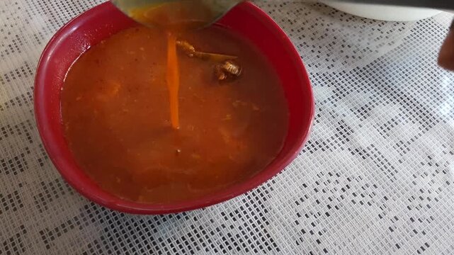 Spoon Stirring Hot Red Beef Broth Stew in Traditional Bowl