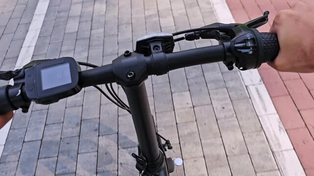 Point-of-view close-up of riding an electric bicycle handlebars on paved path.