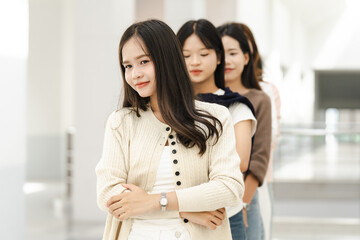Obraz premium Young women stand in a bright, modern hallway. One smiles softly while the others look forward. Their expressions suggest quiet confidence or casual camaraderie. Ideal for lifestyle, fashion