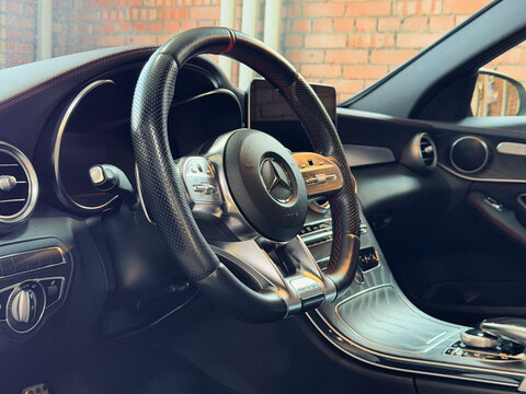 Interior details of a luxury modern Mercedes-AMG C 43 sports sedan. Close-up of the leather performance steering wheel with AMG logo, dashboard, carbon fiber trim, and aluminum pedals.