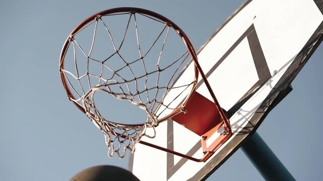 Basketball Scoring Through Hoop Against Clear Blue Sky Outdoors