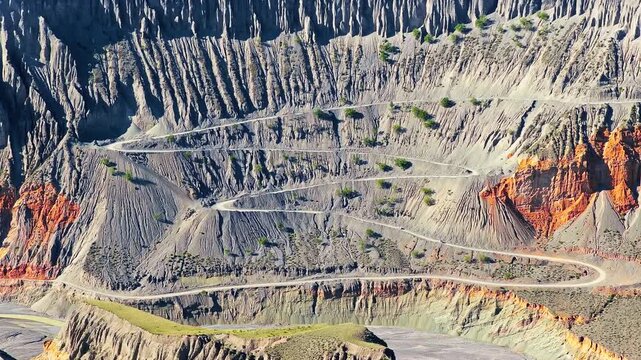 Aerial view of winding mountain road carved through steep eroded canyon cliffs in Dushanzi Grand Canyon, Xinjiang, China.