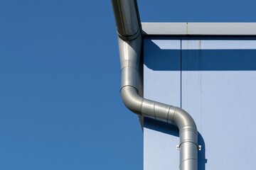 Naklejka premium Modern metal downspout and gutter system on a blue building facade showing architectural details for roof drainage and home exterior maintenance