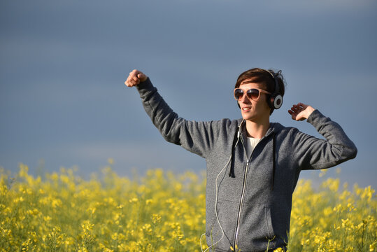 Woman with headphones listening to music in a yellow canola flower field