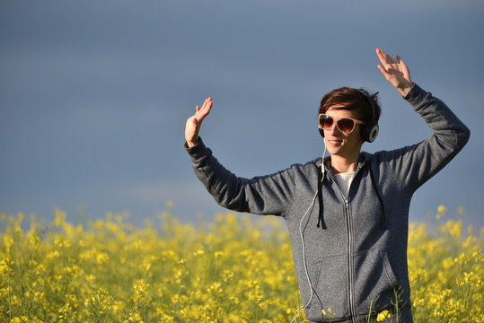 Woman with headphones listening to music in a yellow canola flower field