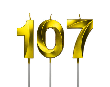 Gold number 107 birthday candles with wicks and white sticks on a white background