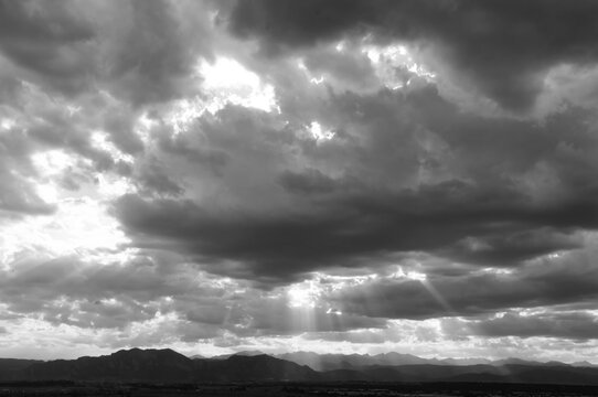 panoramic black and white photo of striking sunset with crepuscular rays over  the boulder flatirons and the front range of the colorado rocky mountains, as seen from broomfield, colorado