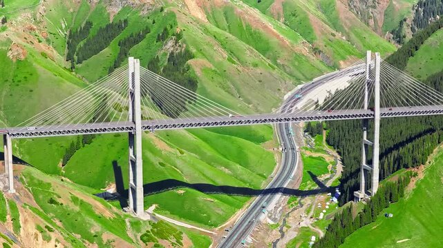 Aerial view of Guozigou Bridge spanning mountain valley in Xinjiang, China, showcasing modern transportation infrastructure against green hillside landscape.