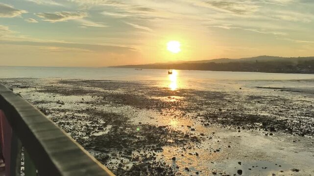 Golden sunset reflecting on low tide tropical sea with distant boat and coastline at dusk. 4K Video