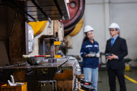 Close-up of an industrial press machine during inspection while engineers discuss production and equipment performance in the background. The image represents preventive maintenance