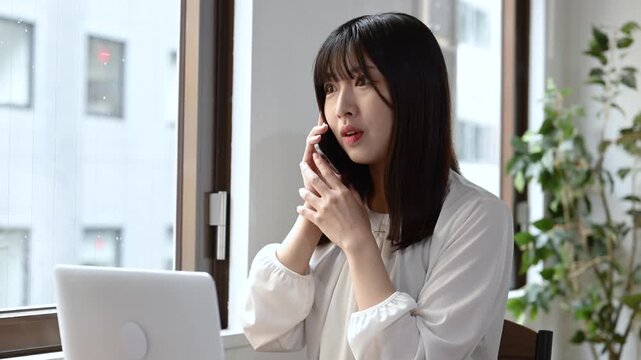 スマートフォンで通話をしながらノートパソコンで仕事をする女性