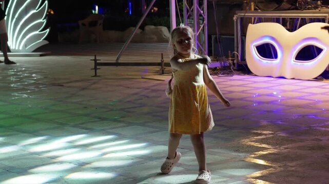 A little girl emotionally and impulsively dances in front of the stage at an adult concert. A happy child on summer vacation at a resort.