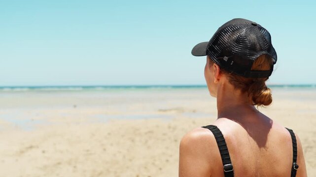 A woman in a swimsuit stands longingly on a sandy beach and watches the turquoise waters ebb in the sea.  The concept of tourist destinations.