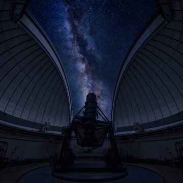 Large astronomical observatory telescope inside open dome aimed at bright milky way galaxy stars in night sky
