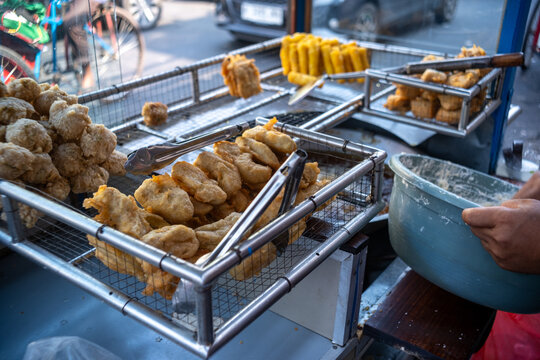 Assorted deep-fried snacks displayed in wire mesh racks on a street food cart, showcasing a selection of popular Indonesian street food.