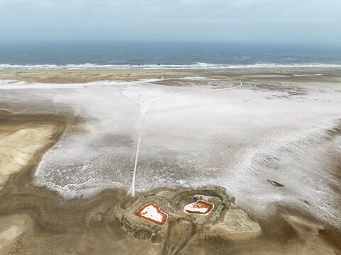 Saline ponds with ruddy algae growth and white salt deposits at the Atlantic Coast. Aerial view. Drone shot. Namib Desert, Skeleton Coast, Dorob National Park, Namibia