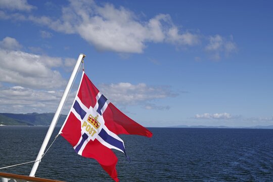 A Norwegian flag blowing in the wind over a clear blue sea and sky, mail ships, Havilla, Trondheim, Norway