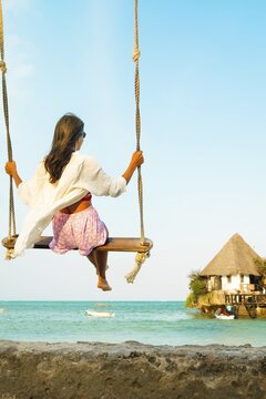 Traveler woman relaxing on swing above south beach in Zanzibar. Leisure tourist travel summer holiday vacation trip. Beautiful destinations place Africa. Happy dream concept