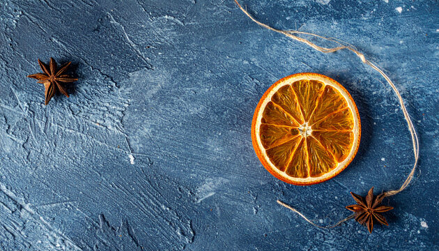 Dried orange slice, star anise, twine, textured blue background, rustic citrus decoration evokes cozy warmth and festive mood