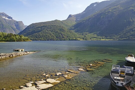A boat is moored on a jetty in a clear mountain lake, surrounded by green mountains, Eikesdalsvatnet, Aursj&ouml;vegen, More og Romsdal, Norway