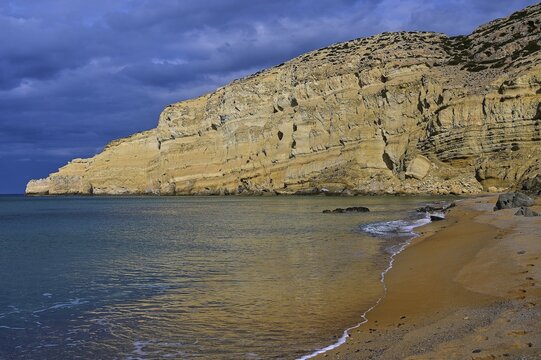 Red Beach, dream beach in the neighboring bay of Matala only accessible on foot, wide coastal landscape with dramatic sky, long-lasting sandy beach and mighty rock face, Matala, Neolithic caves, former hippie paradise, central south coast, Crete, Greek Islands, Greece