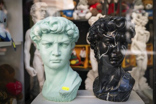 A turquoise and a black bust depicting Michelangelo's David stand in the display case of a souvenir shop, old town, Florence, Tuscany, Italy