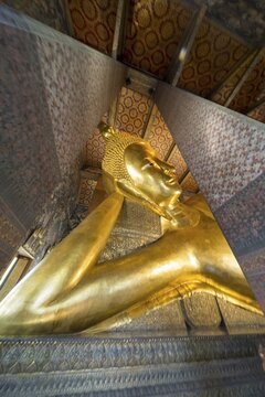 The monumental reclining Buddha shows the moment of entry into Nirvana. Golden surfaces, delicate patterns and warm temple colors accentuate the spiritual peace of this iconic depiction, Wat Pho, Bangkok, Thailand