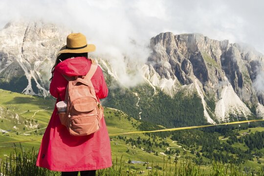 Woman hiker tourist by wooden safety railing fence by mist covered Seceda mountain peaks. Steep cliff edge danger zone. Dolomites Italy. Minimizing human footprint by protecting vulnerable wildlife
