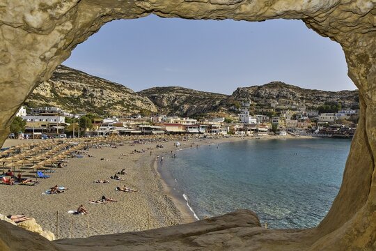 View of a busy beach with umbrellas and a village in the background, Matala, Neolithic caves, former hippie paradise, central south coast, Crete, Greek Islands, Greece