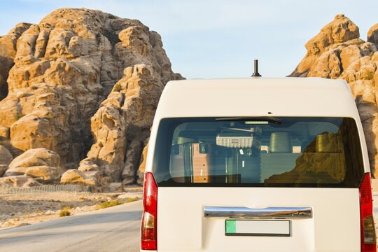 White tourist shuttle minivan full packed rear back view luggage suitcases visible trunk glass driving desert asphalt road sandstone mountains backdrop transportation logistics Jordan Middle East