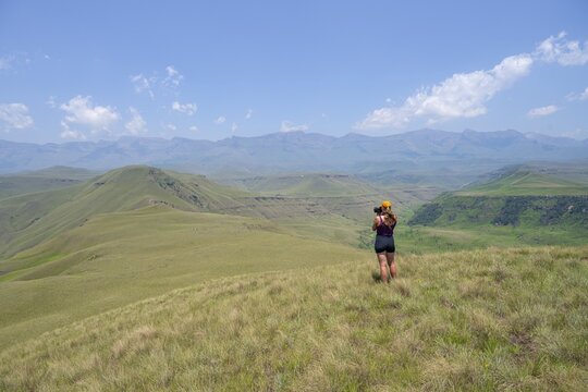 Green hills and valleys, young woman photographing landscape, Worlds View Hike, Drakensberg, South Africa